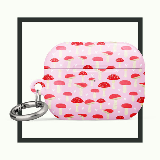 An AirPods® case featuring a whimsical red and white mushroom pattern on a pastel pink background. The case includes a metal carabiner for easy carrying and provides stylish, impact-absorbing protection. Perfect for nature lovers and playful designs!